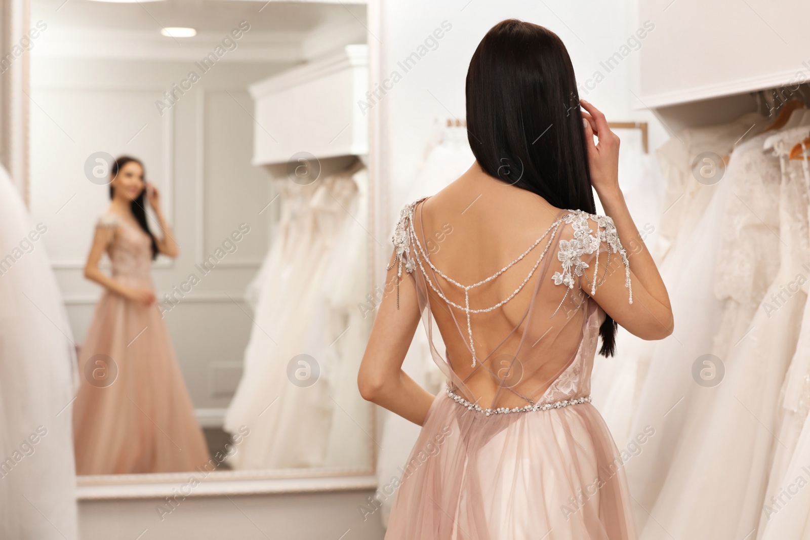 Photo of Woman trying on beautiful wedding dress in boutique, back view