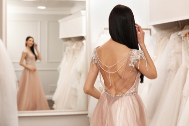 Photo of Woman trying on beautiful wedding dress in boutique, back view