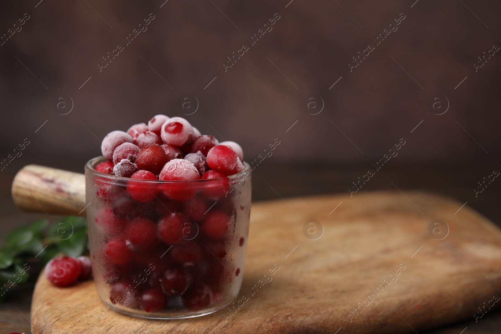 Photo of Frozen red cranberries in glass pot on table, closeup. Space for text