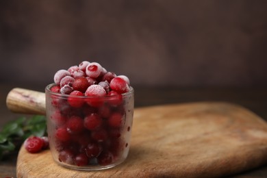 Photo of Frozen red cranberries in glass pot on table, closeup. Space for text