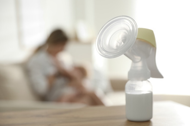 Photo of Mother feeding her little baby at home, focus on breast pump with milk. Healthy growth
