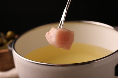 Photo of Dipping piece of raw meat into oil in fondue pot on black background, closeup
