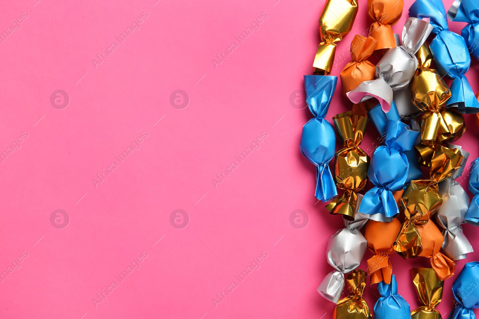 Photo of Candies in colorful wrappers on pink background, flat lay. Space for text