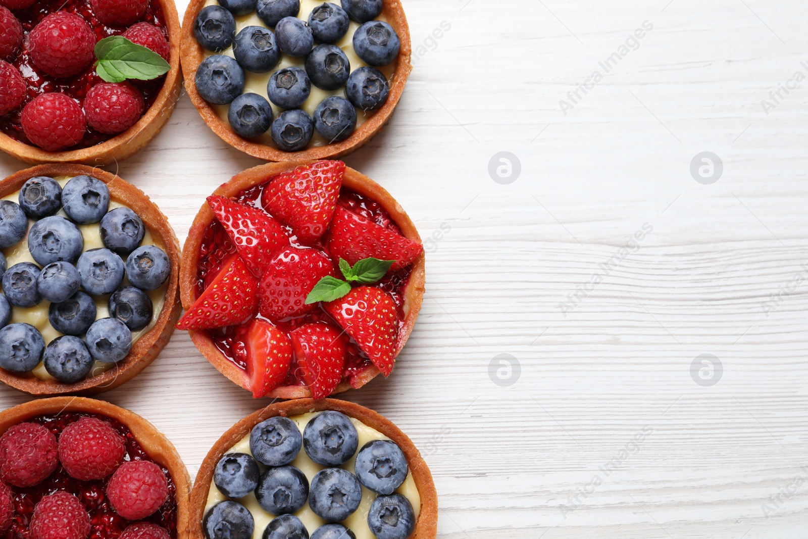 Photo of Tartlets with different fresh berries on white wooden table, flat lay and space for text. Delicious dessert