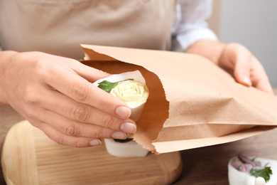 Woman putting natural handmade soap into paper bag at wooden table, closeup