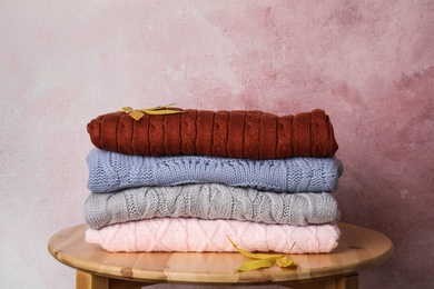 Photo of Stack of knitted clothes on wooden table against pink background. Cozy autumn