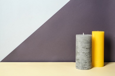 Decorative wax candles on table against color background