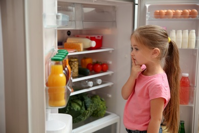 Cute little girl choosing food in refrigerator at home