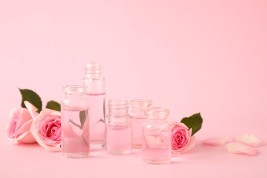 Photo of Bottles of essential oil and roses on pink background. Space for text