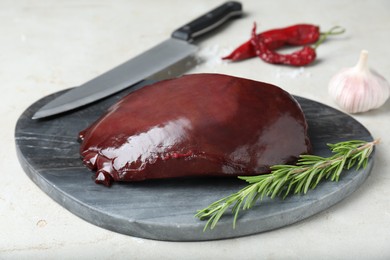 Photo of Piece of raw beef liver with rosemary on light table, closeup