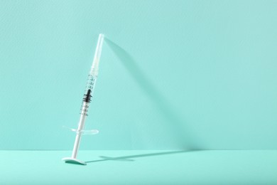 Photo of Cosmetology. Medical syringe on turquoise background, space for text
