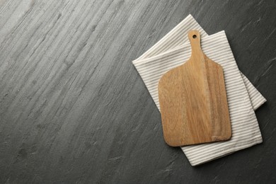 Photo of Wooden cutting board and kitchen towel on dark grey table, top view. Space for text