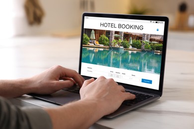 Image of Man using laptop to book hotel at white table, closeup