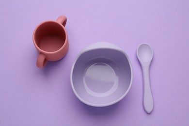 Set of plastic dishware on violet background, flat lay. Serving baby food