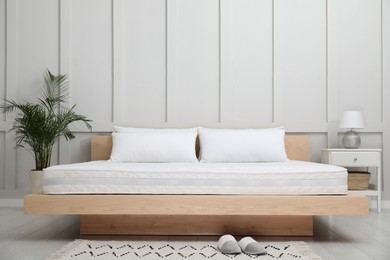 Wooden bed with soft white mattress and pillows in cozy room interior