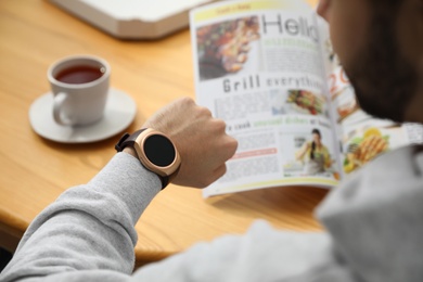 Man checking time on smart watch at table, closeup