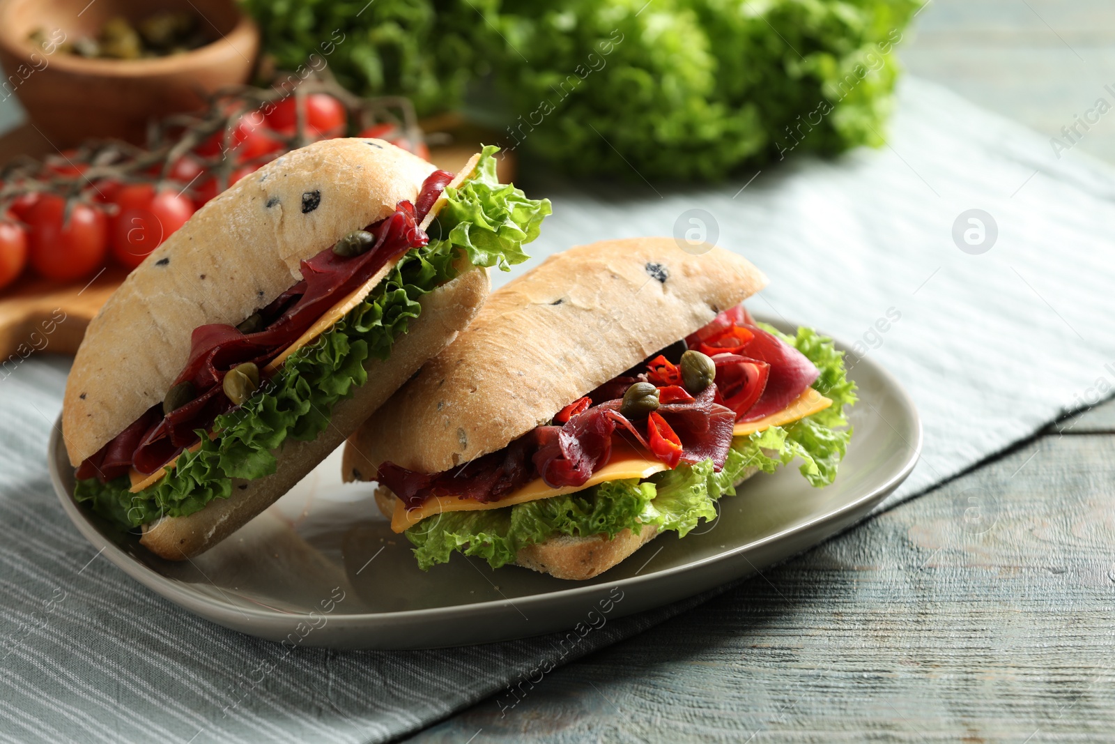 Photo of Delicious sandwiches with bresaola, cheese and lettuce on light blue wooden table