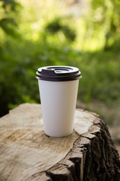 Photo of Takeaway cardboard coffee cup with plastic lid on stump outdoors