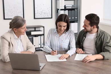 Photo of Young couple consulting insurance agent about pension plan at wooden table indoors