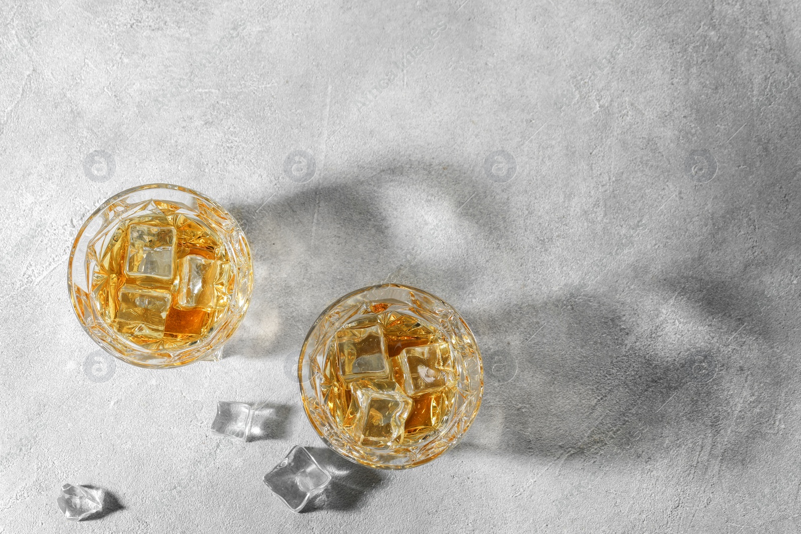 Photo of Whiskey in glasses with ice cubes on grey textured table, flat lay. Space for text