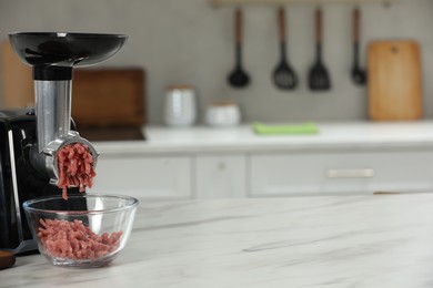 Photo of Electric meat grinder with beef mince on white table in kitchen, space for text