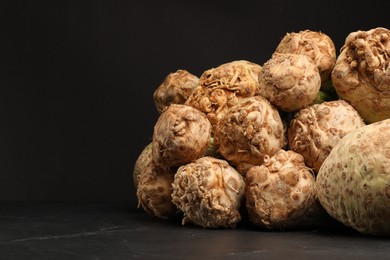 Fresh raw celery roots on black table. Space for text