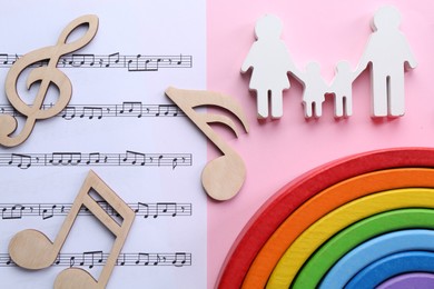 Photo of Baby songs. Music sheet, figures of family, wooden notes and toy rainbow on pink background, flat lay