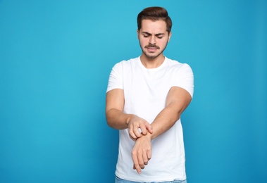 Photo of Young man scratching arm on color background. Annoying itch