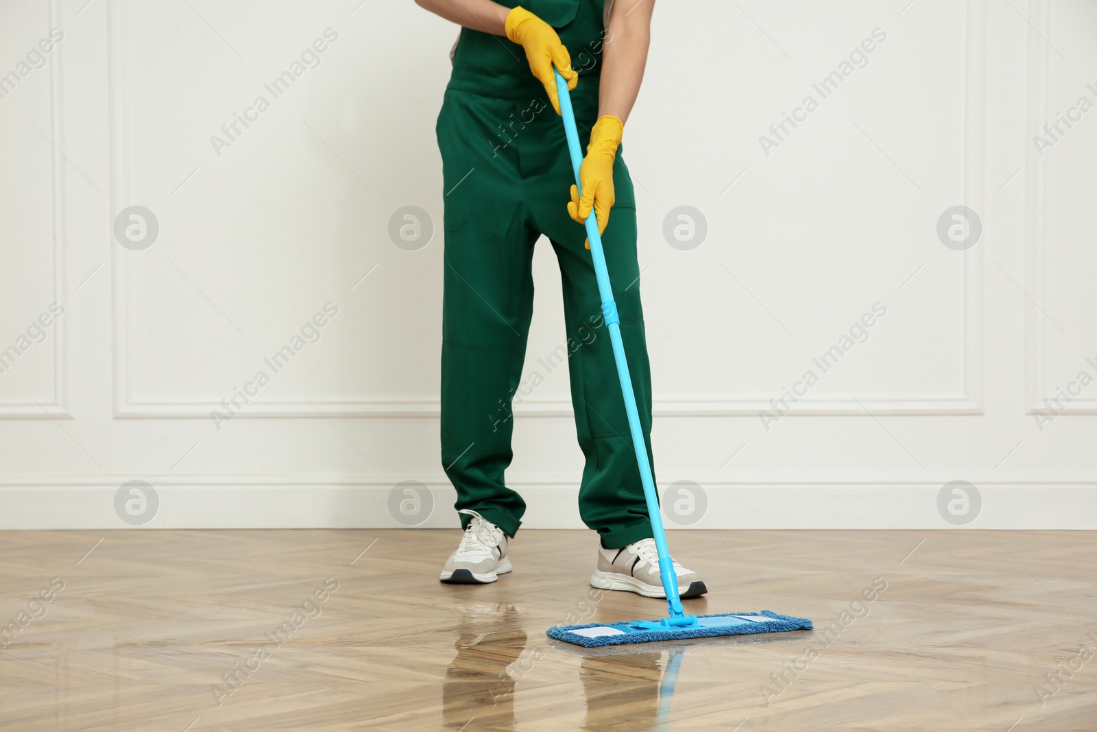 Photo of Professional janitor cleaning parquet floor with mop indoors, closeup
