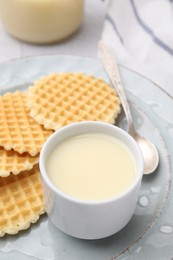 Photo of Tasty condensed milk and waffles on table, closeup