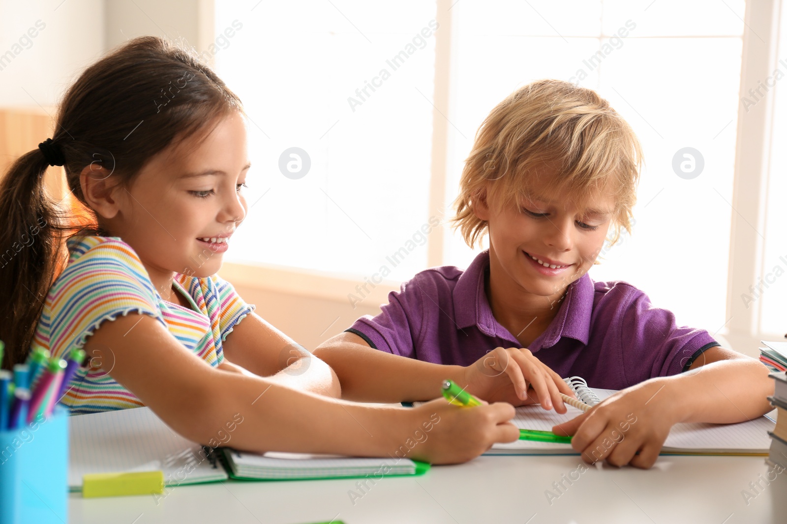 Photo of Little boy and girl doing homework at table indoors