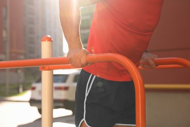 Photo of Man training on parallel bars at outdoor gym on sunny day, closeup