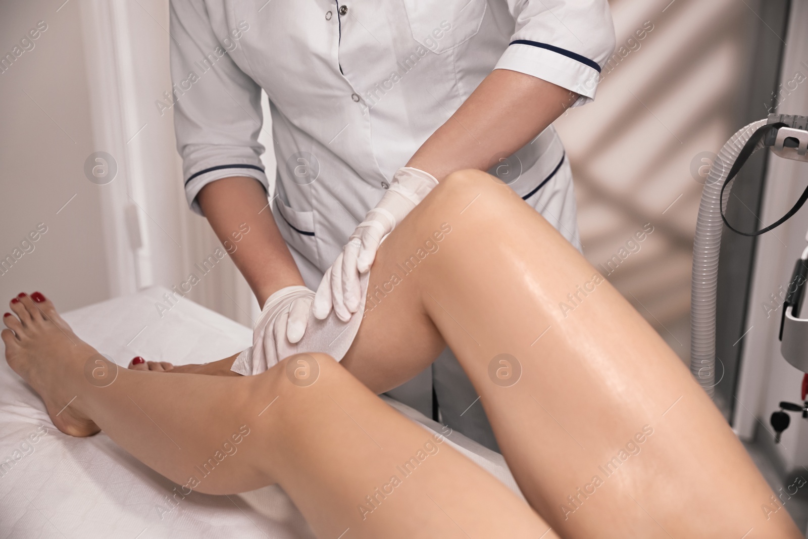 Photo of Professional cosmetologist removing gel from client's leg after laser epilation procedure in salon, closeup