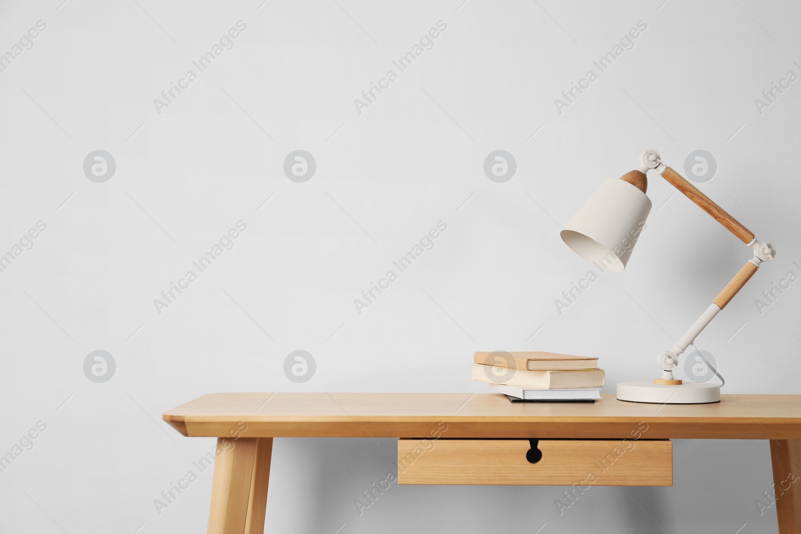 Photo of Stylish modern desk lamp and books on wooden table near white wall