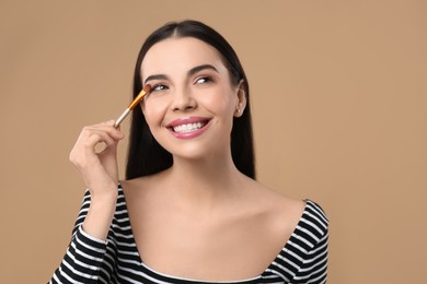 Photo of Beautiful woman applying makeup on light brown background