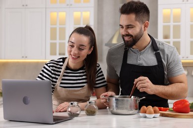 Photo of Happy lovely couple using laptop while cooking in kitchen