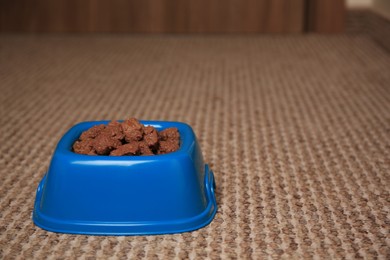 Photo of Wet pet food in feeding bowl on soft carpet indoors. Space for text