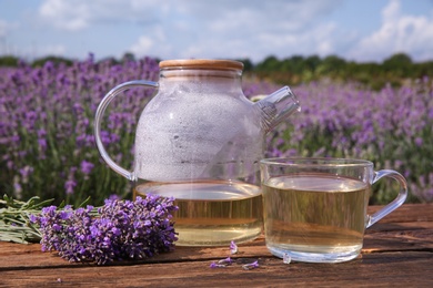 Photo of Tasty herbal tea and fresh lavender flowers on wooden table in field, closeup