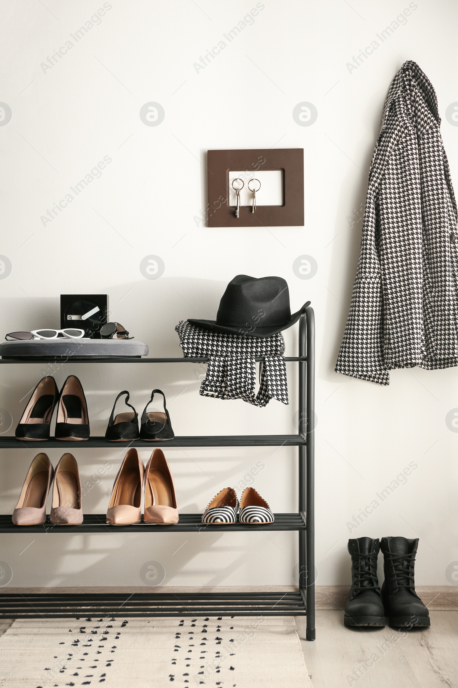 Photo of Black shelving unit with shoes and different accessories near white wall in hall