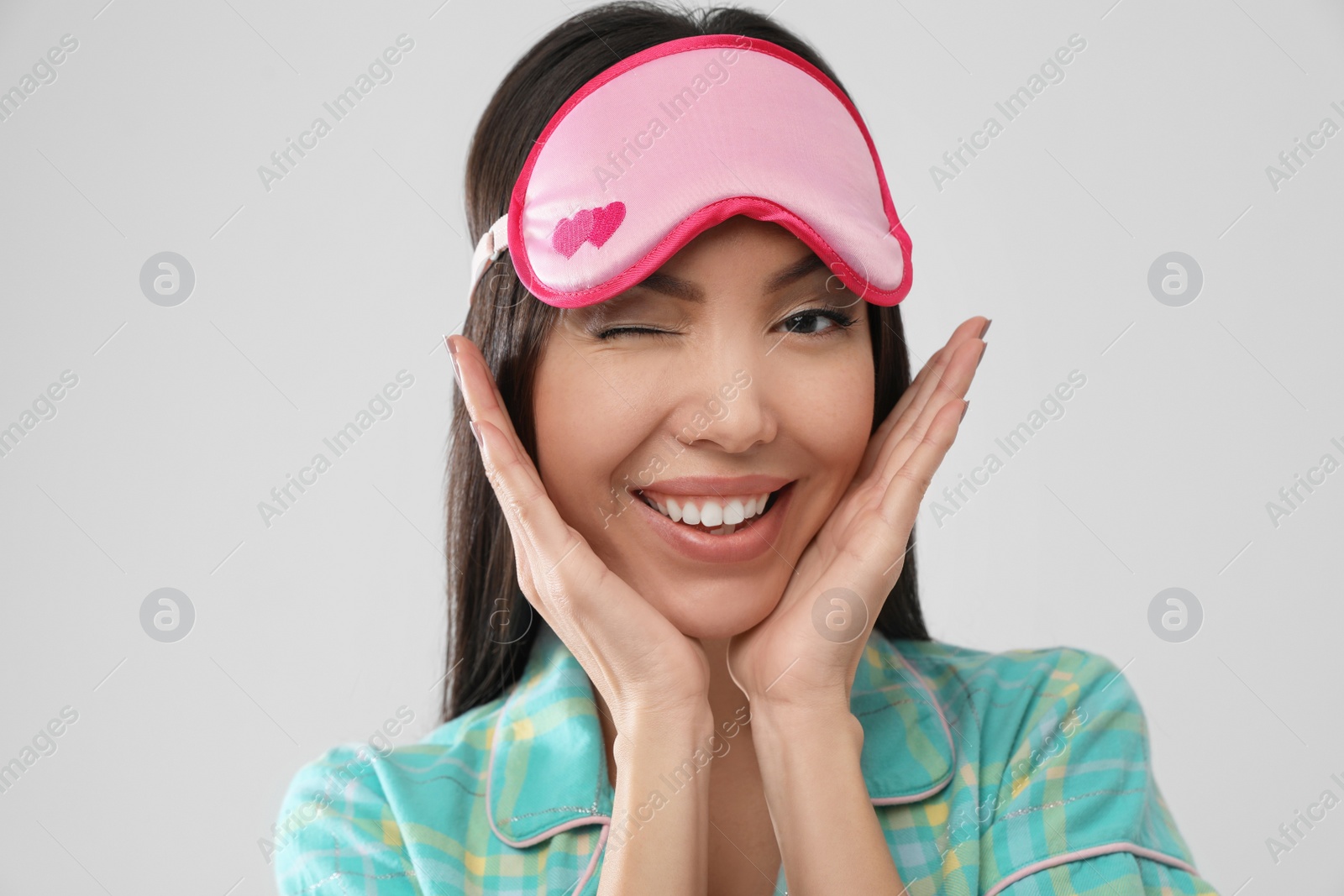 Photo of Beautiful Asian woman wearing pajamas and sleeping mask on light grey background. Bedtime