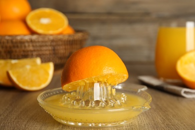 Photo of Squeezer and cut fresh oranges on wooden table, closeup