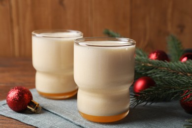 Photo of Glasses of delicious eggnog and decorated fir branch on wooden table