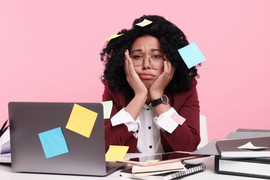 Photo of Stressful deadline. Portrait of exhausted woman sitting at white table against pink background. Many sticky notes everywhere as reminders