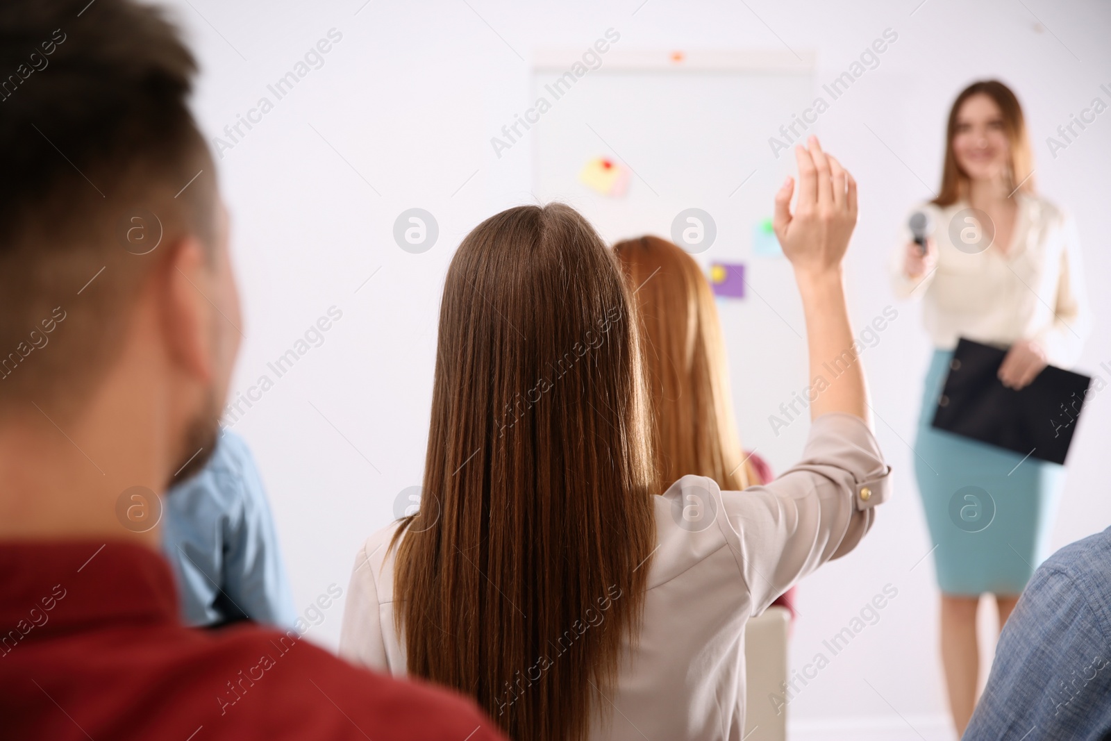 Photo of Young woman raising hand to ask question at business training indoors, back view