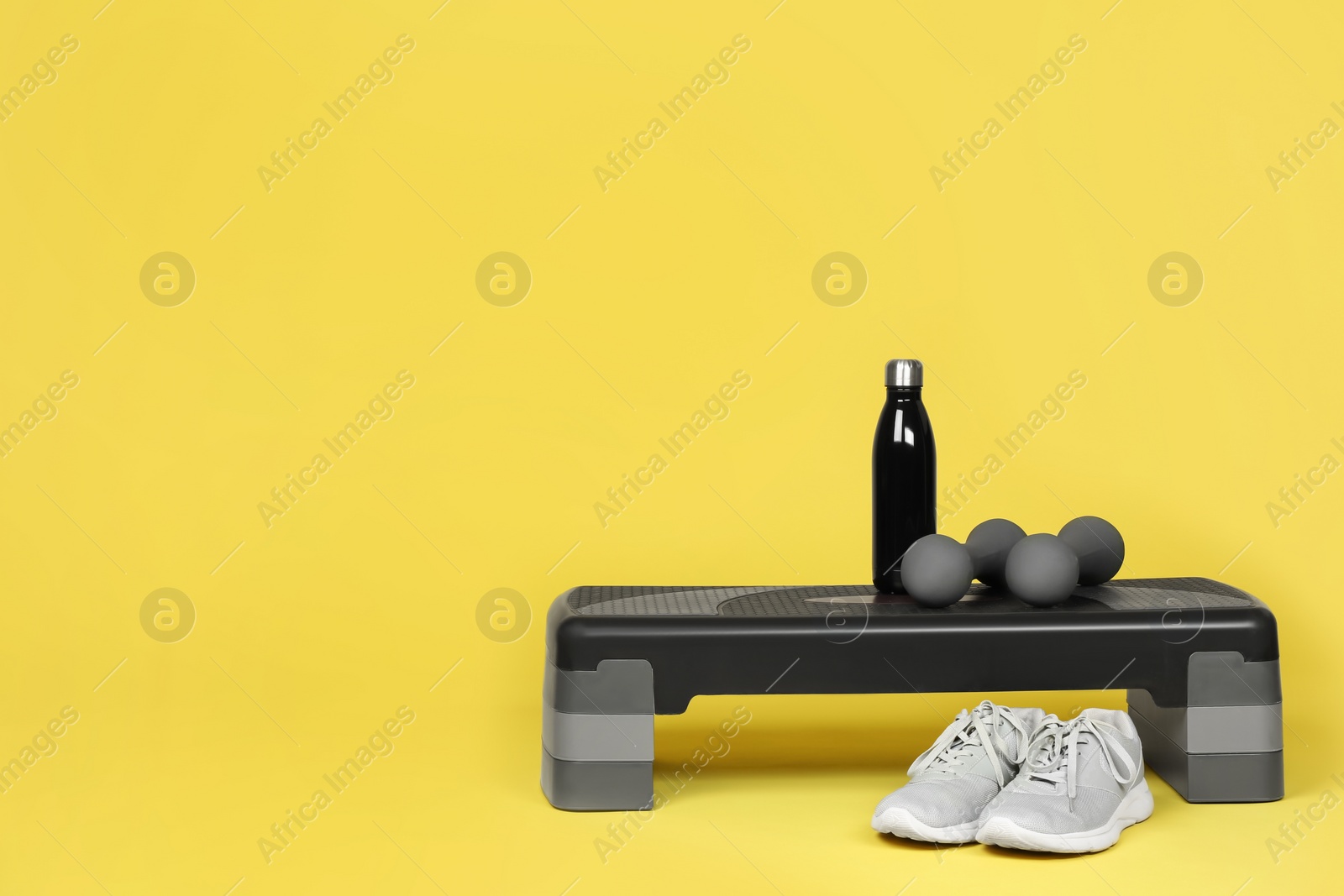 Photo of Step platform, dumbbells, water bottle and sneakers on yellow background, space for text. Sport equipment