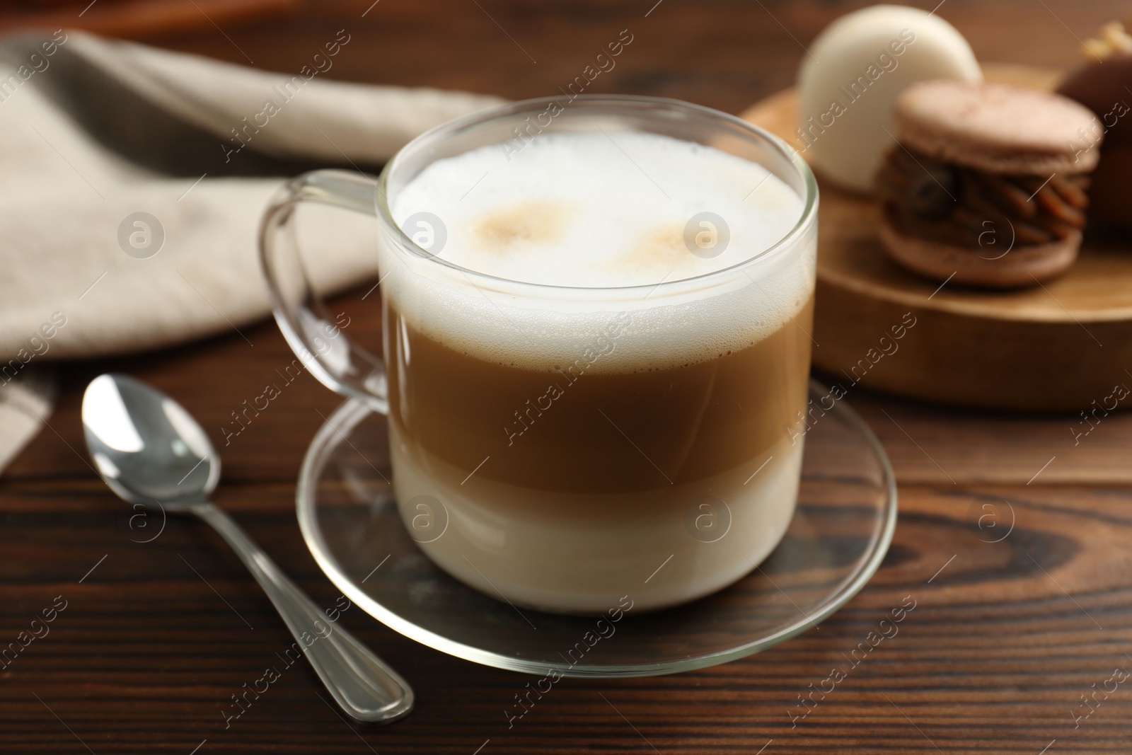 Photo of Aromatic coffee in cup, spoon and macarons on wooden table, closeup