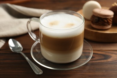 Photo of Aromatic coffee in cup, spoon and macarons on wooden table, closeup