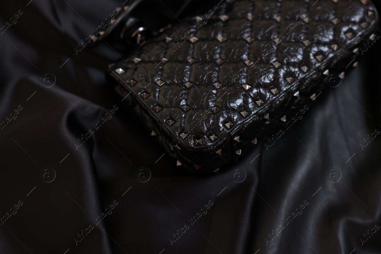 Photo of Stylish leather bag on black silk, closeup. Space for text