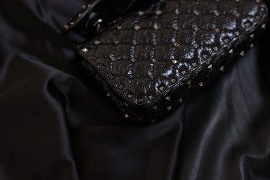 Stylish leather bag on black silk, closeup. Space for text