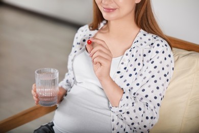 Photo of Pregnant woman holding pill and glass of water indoors, closeup